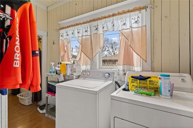 clothes washing area with wood finished floors, washing machine and dryer, laundry area, and wood walls