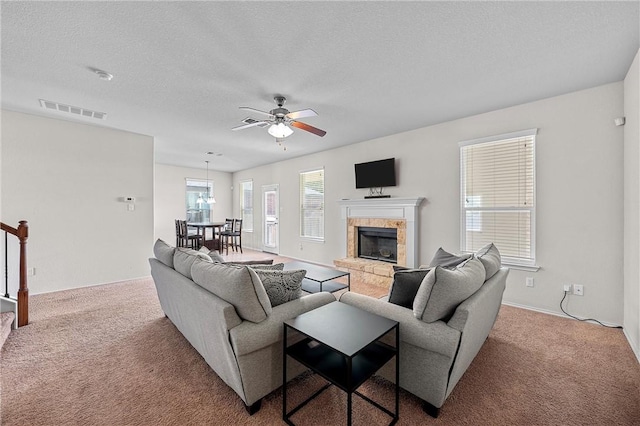 carpeted living room featuring ceiling fan, a fireplace, and a textured ceiling