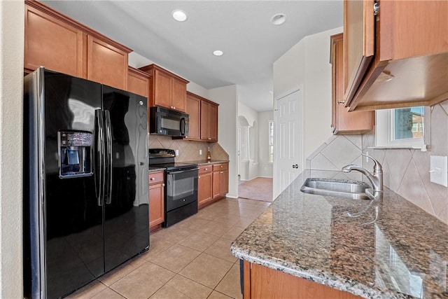 kitchen with sink, dark stone countertops, decorative backsplash, light tile patterned flooring, and black appliances