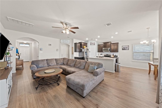 living area with arched walkways, ceiling fan with notable chandelier, light wood-type flooring, and visible vents