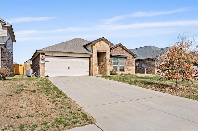 single story home with driveway, a garage, stone siding, central air condition unit, and brick siding