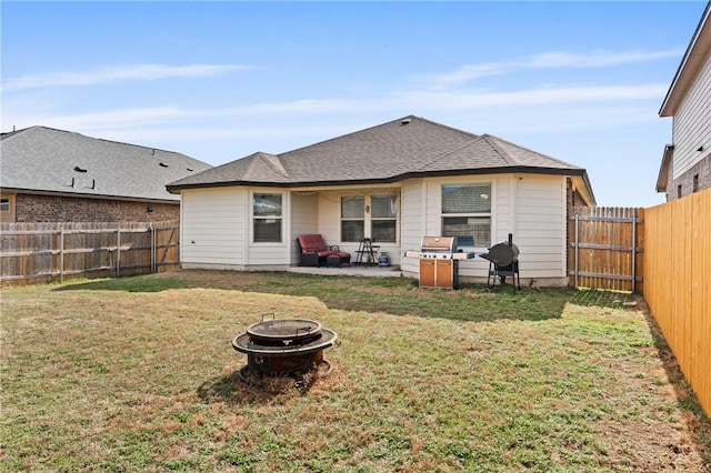 rear view of house featuring a yard, a shingled roof, a patio area, a fenced backyard, and a fire pit