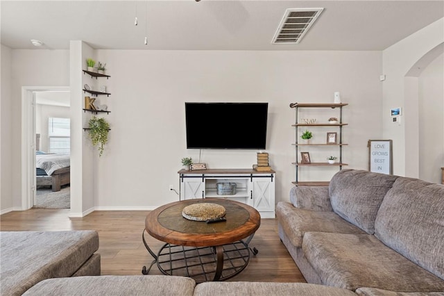 living area with arched walkways, visible vents, baseboards, and wood finished floors