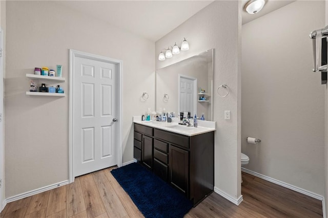 bathroom with double vanity, baseboards, toilet, wood finished floors, and a sink