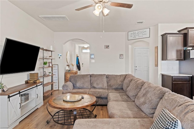 living area featuring light wood-style floors, visible vents, arched walkways, and a ceiling fan