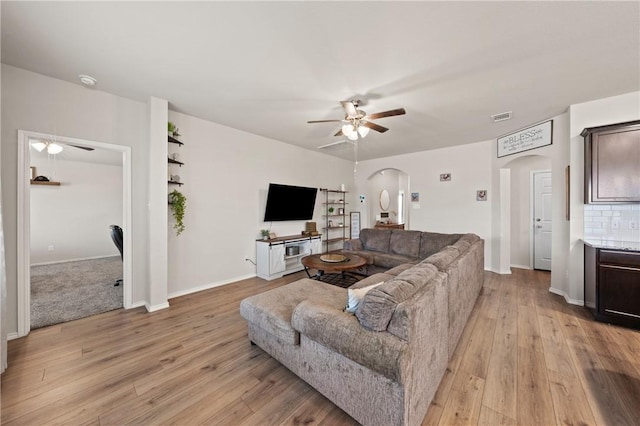 living area featuring arched walkways, ceiling fan, visible vents, and light wood-style floors