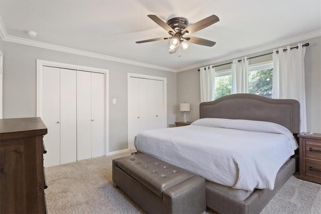 carpeted bedroom featuring ceiling fan, crown molding, and two closets