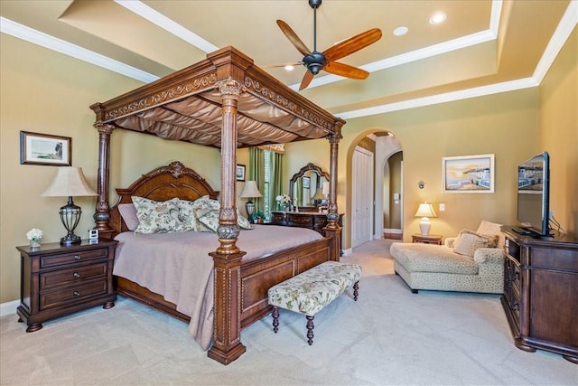 carpeted bedroom featuring baseboards, arched walkways, a raised ceiling, ceiling fan, and crown molding