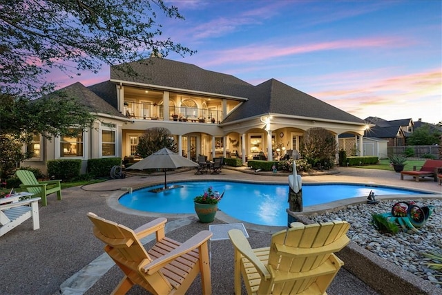 pool at dusk with a patio, a storage unit, fence, an outdoor pool, and an outdoor structure