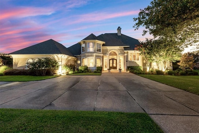 french country style house featuring concrete driveway, a lawn, and a chimney