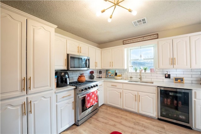 kitchen with wine cooler, sink, white cabinetry, light wood-type flooring, and appliances with stainless steel finishes