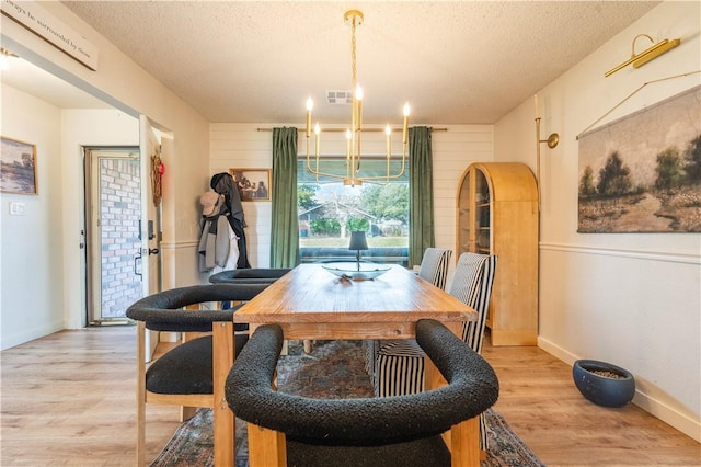 dining room with an inviting chandelier, light hardwood / wood-style floors, and a textured ceiling