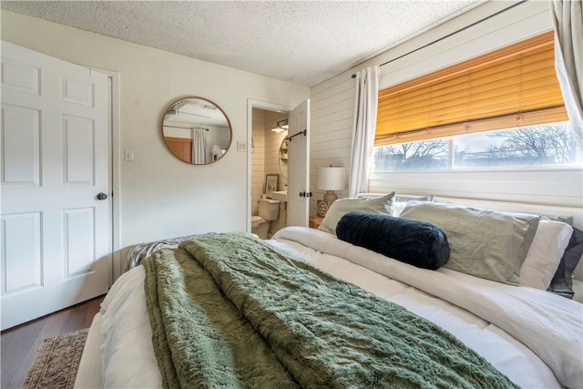 bedroom with dark wood-type flooring, a textured ceiling, and ensuite bath