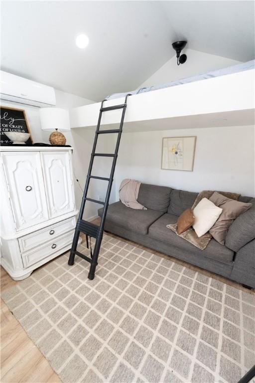 living room featuring vaulted ceiling, a wall mounted AC, and light wood-type flooring