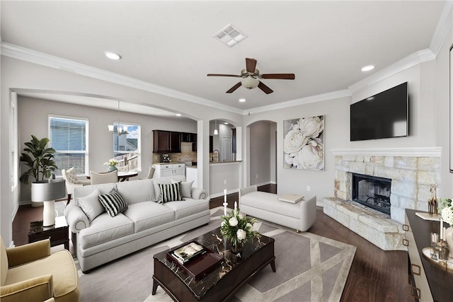 living room with hardwood / wood-style floors, ceiling fan with notable chandelier, a stone fireplace, and ornamental molding