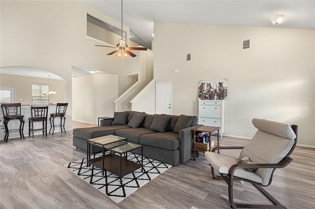 living room featuring ceiling fan with notable chandelier, light hardwood / wood-style flooring, and high vaulted ceiling