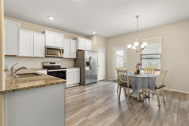 kitchen featuring appliances with stainless steel finishes, light wood-type flooring, sink, pendant lighting, and white cabinetry