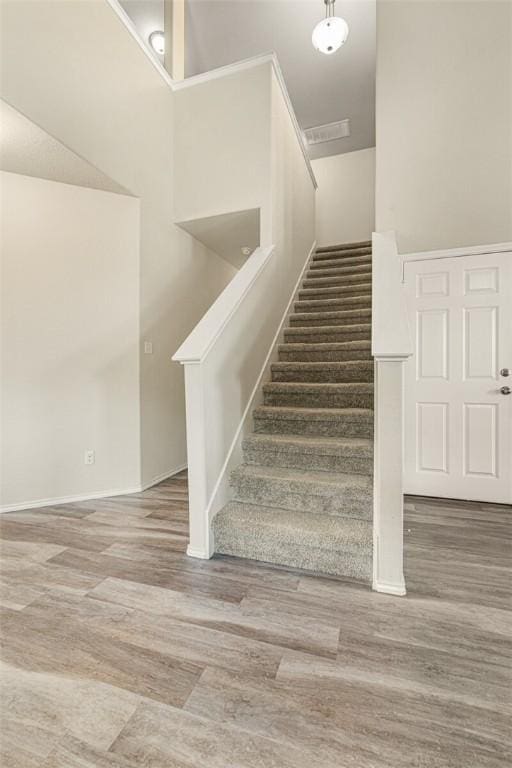 stairway with wood-type flooring and a towering ceiling