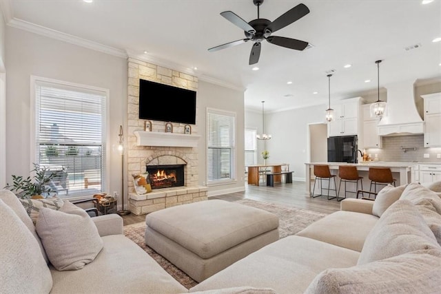 living room with a fireplace, crown molding, light wood finished floors, and ceiling fan with notable chandelier