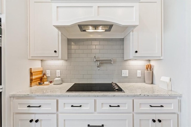 kitchen featuring black electric stovetop, white cabinets, backsplash, custom exhaust hood, and light stone countertops