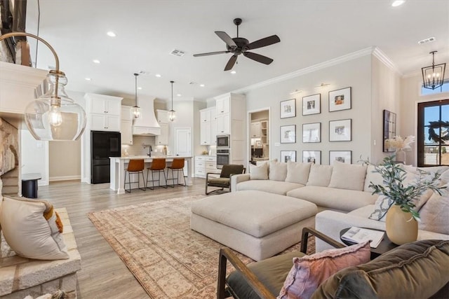 living area featuring recessed lighting, visible vents, ornamental molding, light wood-type flooring, and ceiling fan with notable chandelier