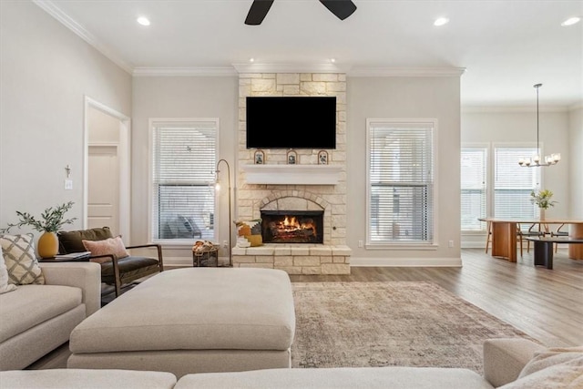 living room featuring wood finished floors, ceiling fan with notable chandelier, crown molding, a fireplace, and recessed lighting