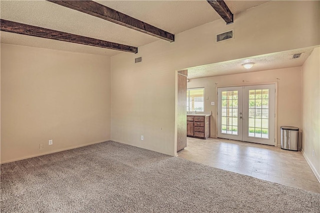 carpeted spare room with french doors, beamed ceiling, and a textured ceiling