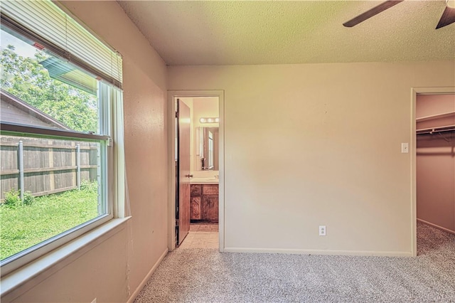 unfurnished bedroom with a walk in closet, a closet, ensuite bath, and multiple windows