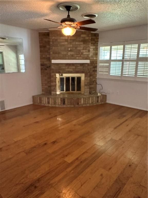 unfurnished living room with ceiling fan, a fireplace, wood-type flooring, and a textured ceiling