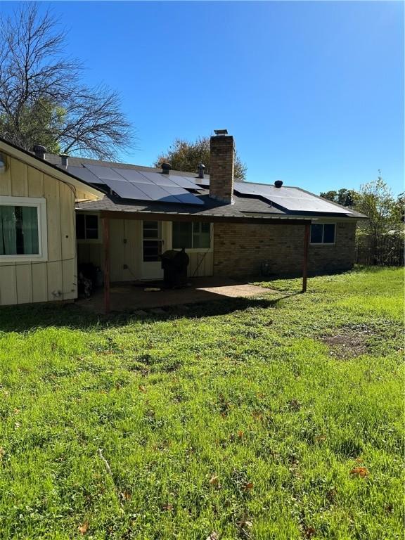 rear view of property with solar panels and a yard