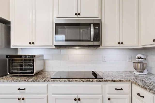 kitchen featuring tasteful backsplash, black electric cooktop, white cabinetry, and light stone countertops