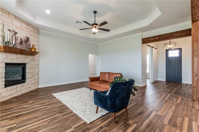 living room with dark hardwood / wood-style floors, a tray ceiling, a fireplace, ceiling fan with notable chandelier, and ornamental molding