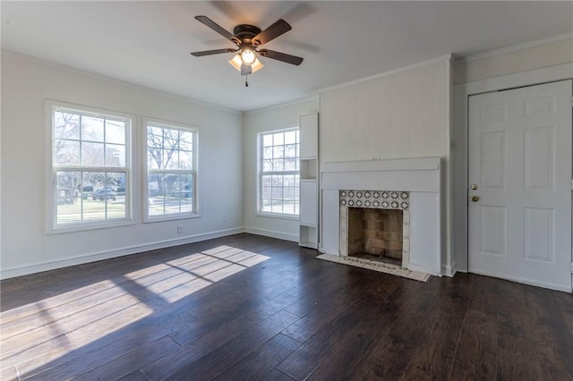 unfurnished living room with baseboards, dark wood finished floors, a tiled fireplace, ceiling fan, and ornamental molding