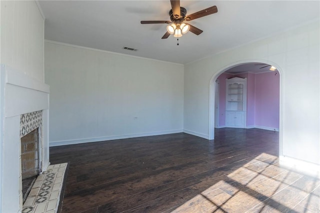 unfurnished living room with crown molding, ceiling fan, dark wood-type flooring, and a tiled fireplace