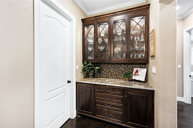 bar featuring decorative backsplash, light stone countertops, dark hardwood / wood-style flooring, dark brown cabinets, and crown molding