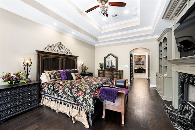 bedroom with ceiling fan, a high end fireplace, dark hardwood / wood-style floors, crown molding, and a tray ceiling