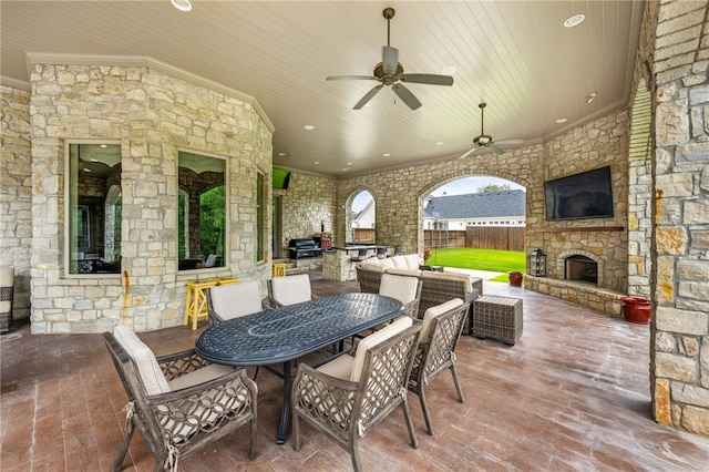 view of patio featuring an outdoor stone fireplace, ceiling fan, and an outdoor kitchen