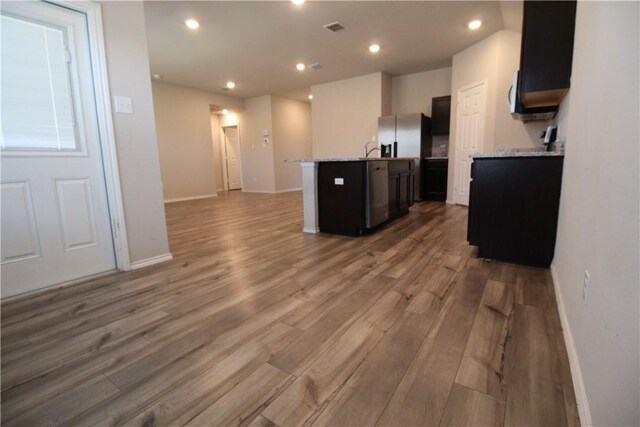 kitchen featuring hardwood / wood-style flooring, sink, light stone counters, and an island with sink