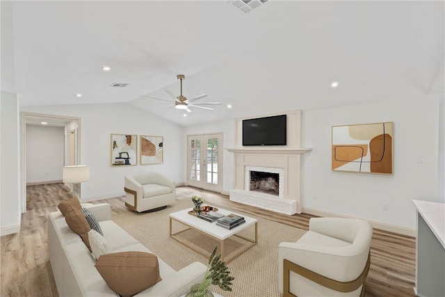 living room featuring ceiling fan, french doors, light hardwood / wood-style floors, vaulted ceiling, and a fireplace