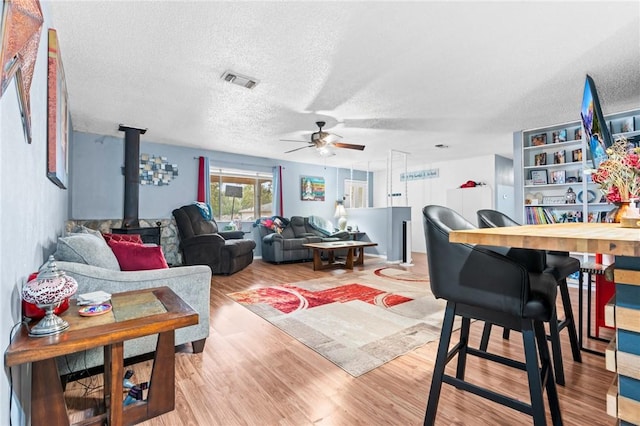 living room featuring wood-type flooring, a textured ceiling, a wood stove, and ceiling fan