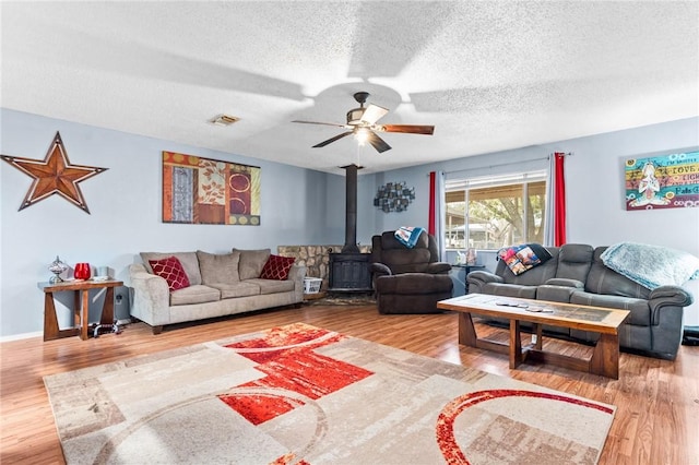 living room with hardwood / wood-style floors, ceiling fan, a wood stove, and a textured ceiling