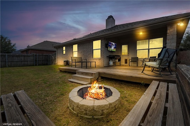 back of property with a deck, an outdoor fire pit, fence, a yard, and a chimney