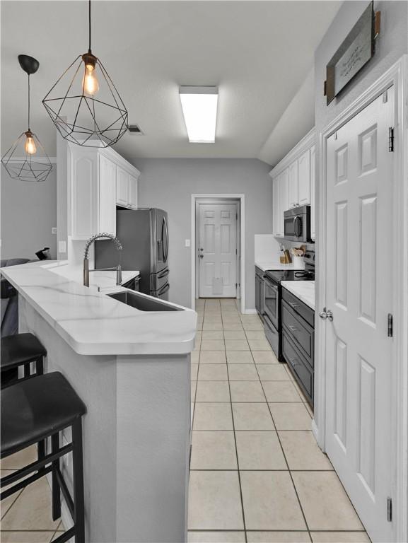 kitchen with appliances with stainless steel finishes, white cabinetry, a peninsula, and light tile patterned flooring