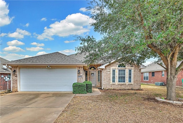 single story home with a garage, driveway, brick siding, and central air condition unit