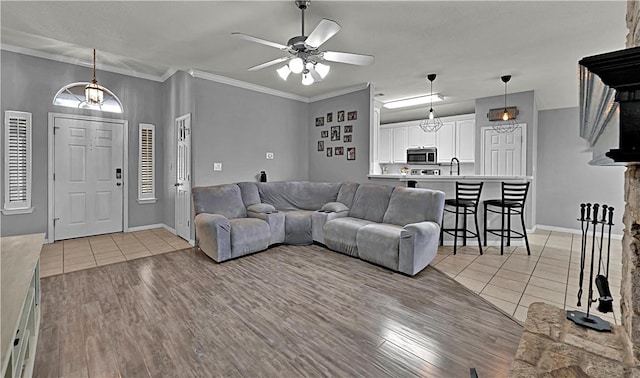 living room with ornamental molding, a ceiling fan, baseboards, and light tile patterned floors