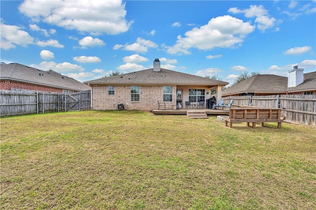 back of house featuring a fenced backyard, brick siding, a yard, a wooden deck, and a chimney