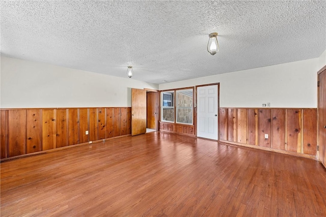 empty room with hardwood / wood-style floors, a textured ceiling, and wooden walls