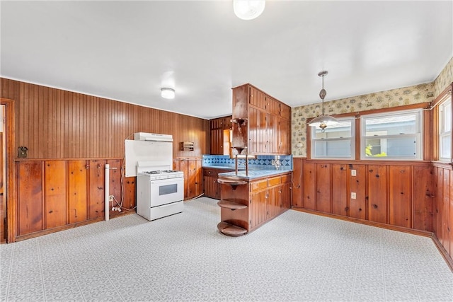 kitchen with kitchen peninsula, tasteful backsplash, white range, pendant lighting, and wood walls