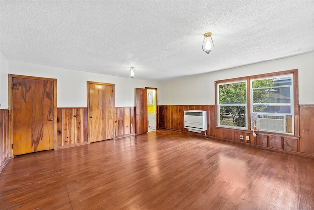 unfurnished living room with heating unit, hardwood / wood-style floors, cooling unit, and a textured ceiling