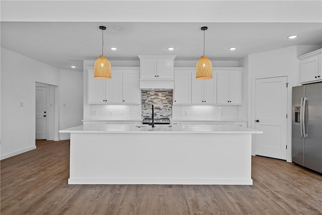 kitchen with stainless steel refrigerator with ice dispenser, light wood-type flooring, a kitchen island with sink, and pendant lighting